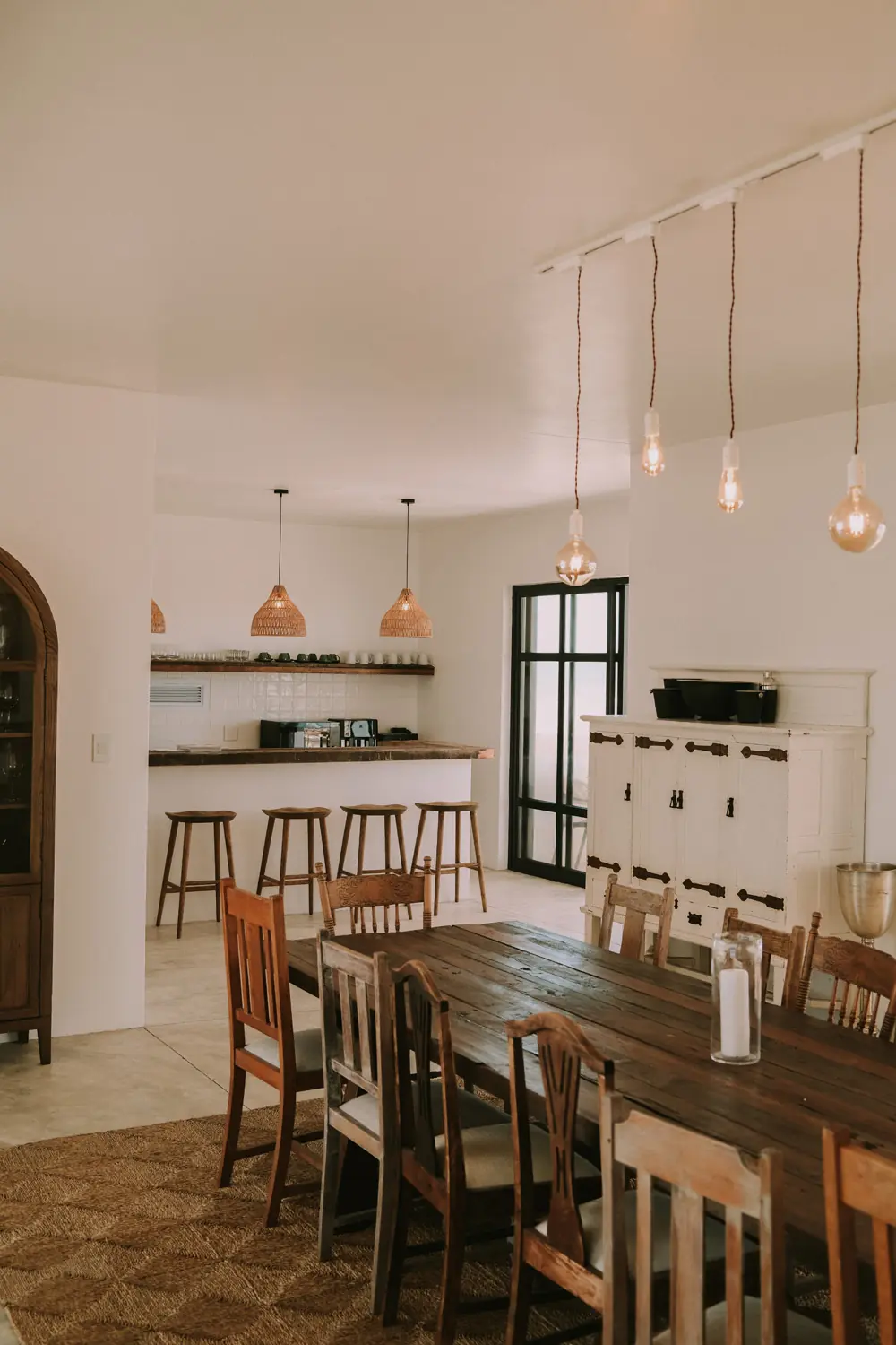 The dining table and the kitchen bar beyond, with rattan pendants and timber stools