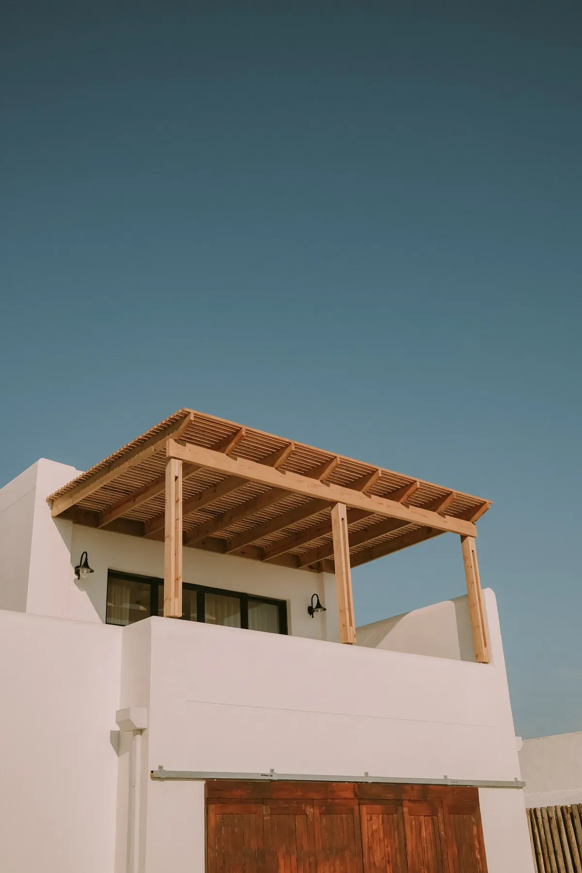 The upper balcony’s timber pergola against a deep blue sky, above a wooden sliding door