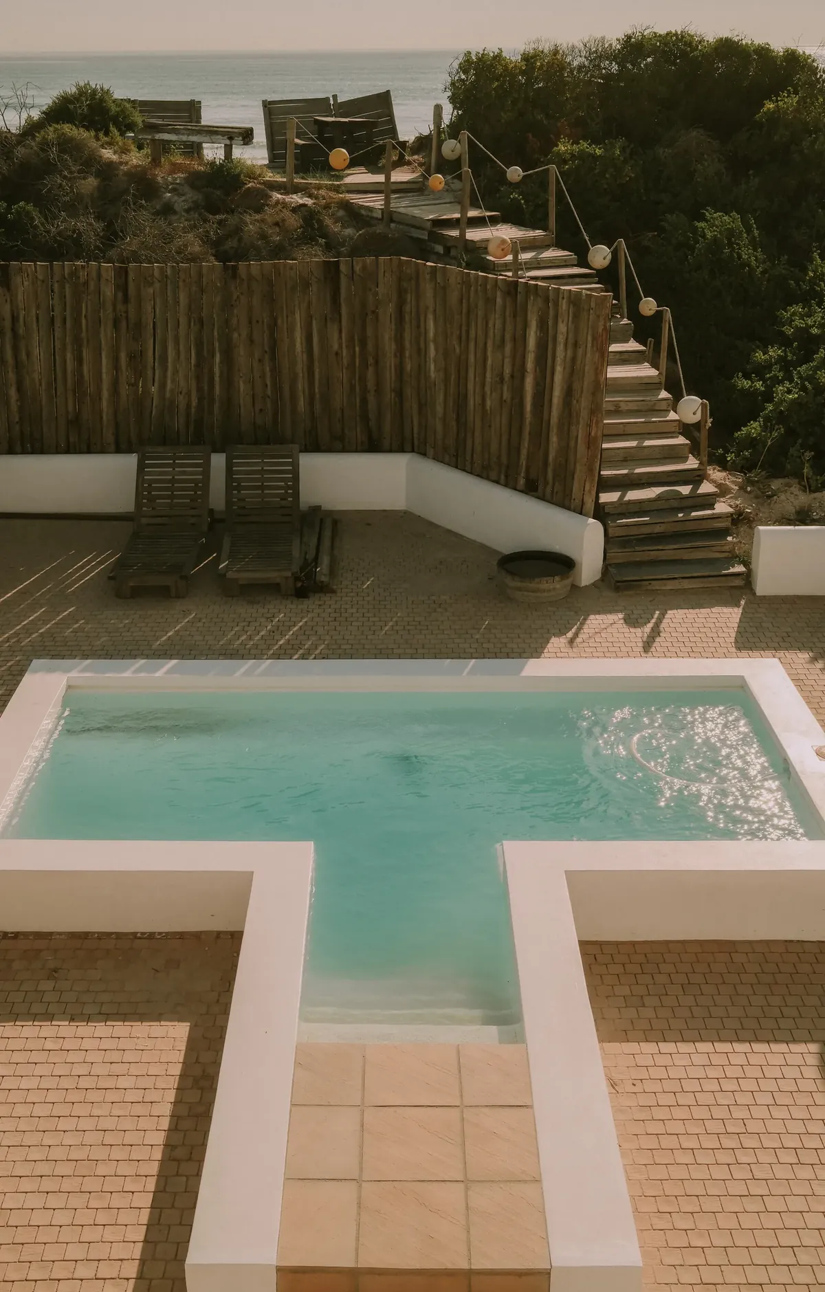 The T-shaped pool and loungers, with timber steps up the dune towards the beach