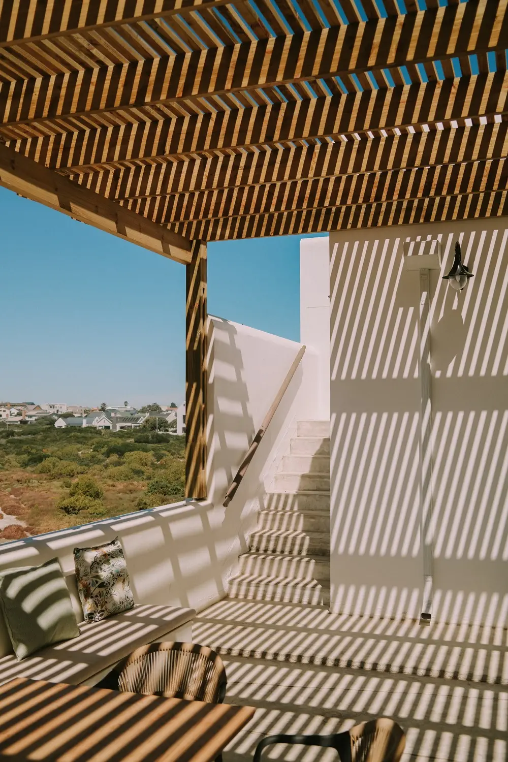 Whitewashed steps and a bench on the terrace, striped with pergola shadows, above the rooftops and marsh